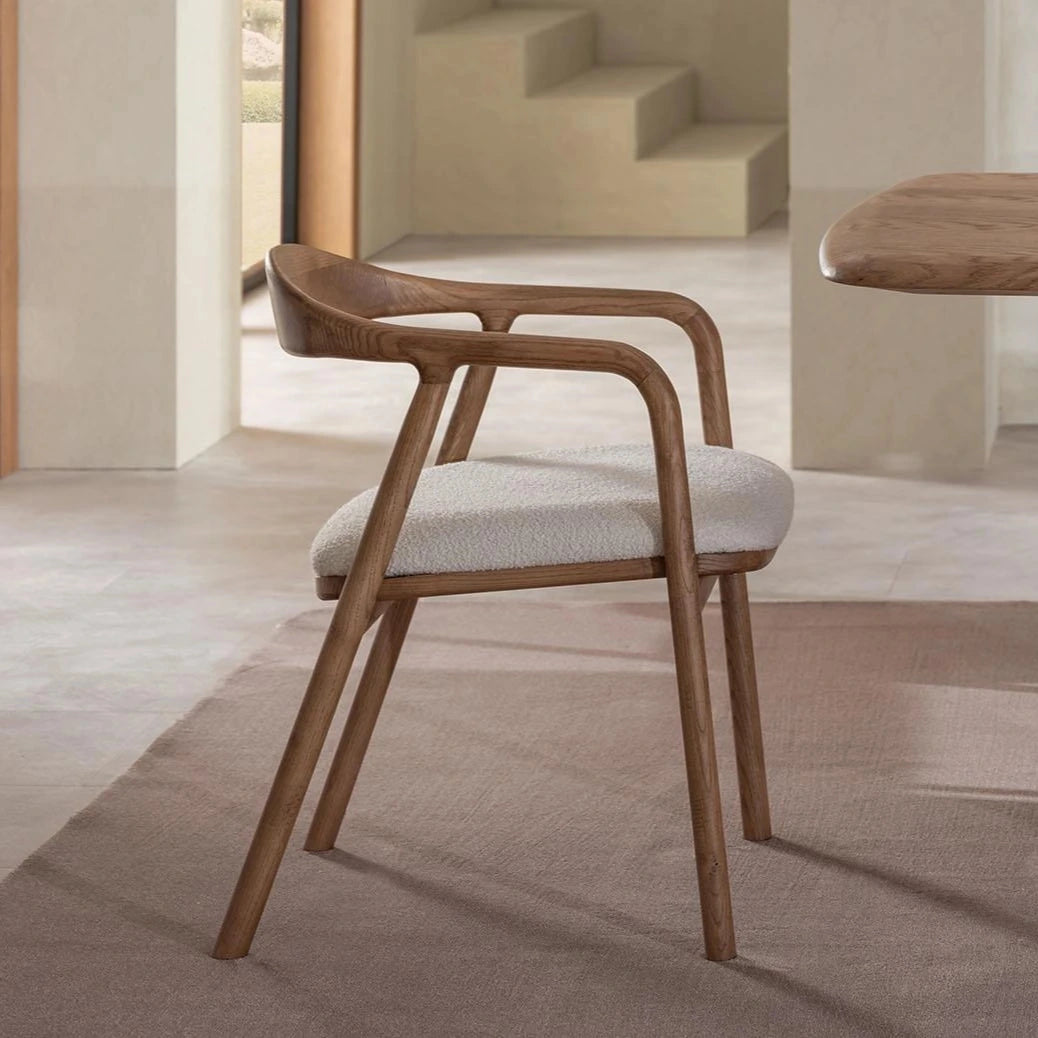 Wooden chair with white cushion next to a wooden table in a minimalistic room.